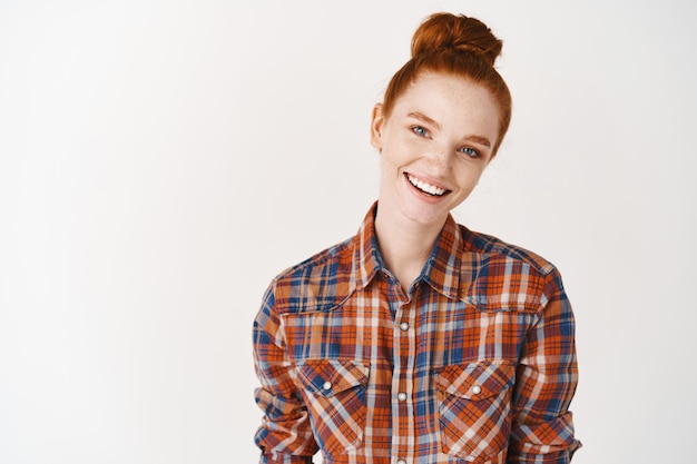 Headshot Portrait of happy ginger girl with freckles smiling looking at front. White wall