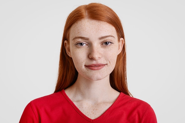 Headshot of pretty freckled redhead female looks with friendly expression at camera