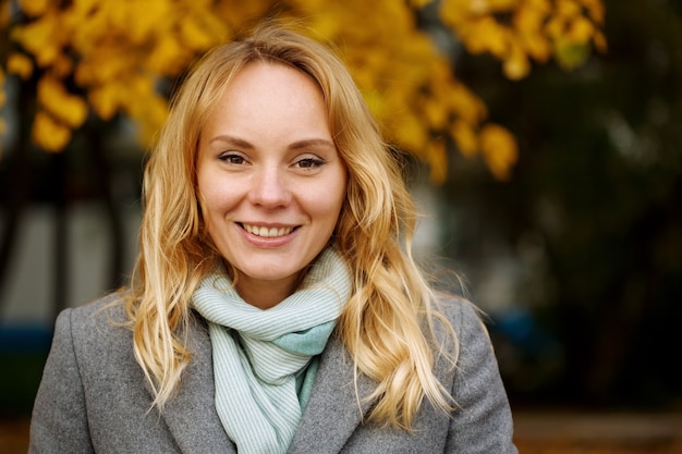 Headshot of pretty smiling blonde woman at the autumn nature with copy space looking at camera