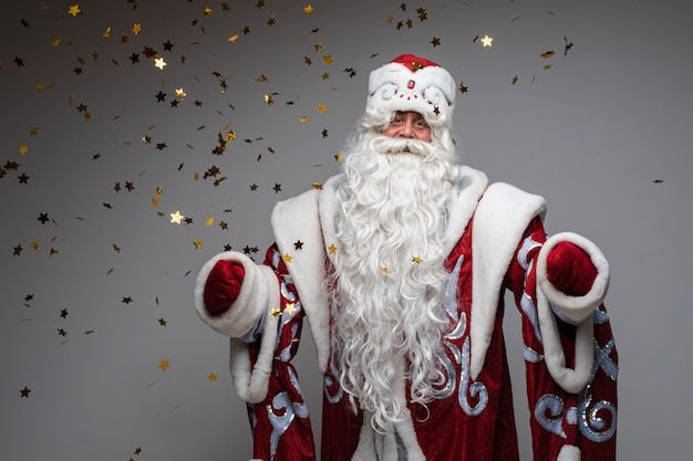 Headshot of Santa Claus in red hat, gray-haired beared tired man on gray studio background. High quality photo