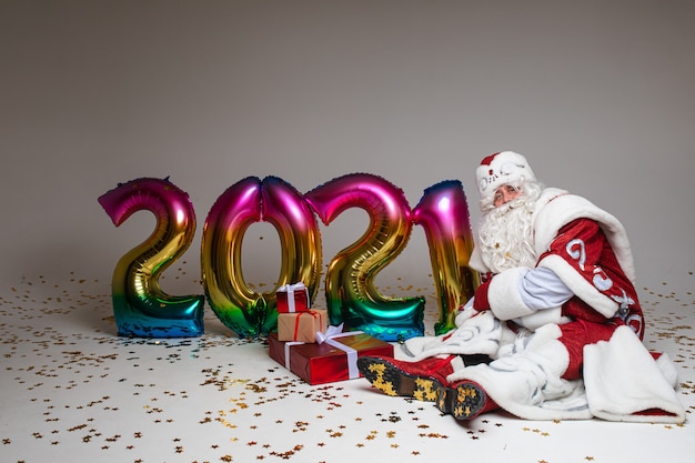 Headshot of Santa Claus in red hat, gray-haired beared tired man on gray studio background. High quality photo