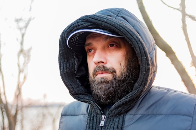 Headshot van een man in een kap. Man in een grijze jas met een capuchon. Een man met een baard.