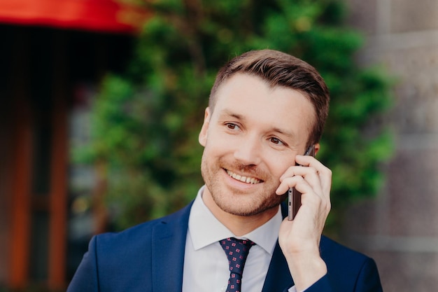 Headshot van knappe ongeschoren jonge man heeft een gesprek met de service-operator heeft een gelukkige uitdrukking aantrekkelijke look gekleed in formele outfit poses buiten mensen en lifestyle concept