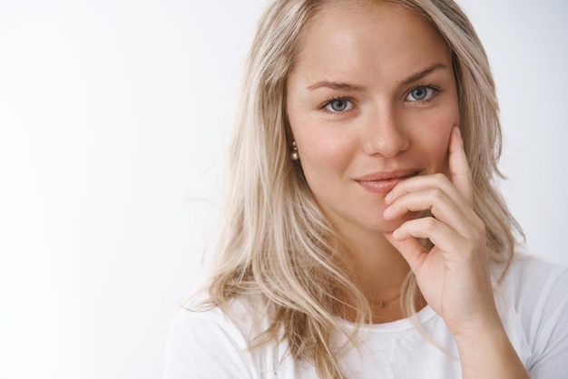 Headshot van tedere en sensuele aantrekkelijke Europese blonde in wit t-shirt verleidelijk aanraken lip flirterig en brutaal lachend op camera poseren vrouwelijk op wit