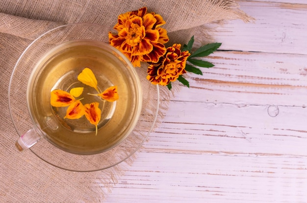 Tè di calendula curativo in una tazza trasparente su uno sfondo di legno bianco