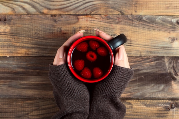 Healing tea with raspberries and berries on the table. A cup in the hands of a girl. Combating colds in winter by natural methods.