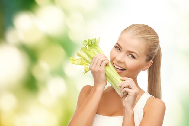 healtcare, food and diet concept - smiling woman biting piece of celery or green salad