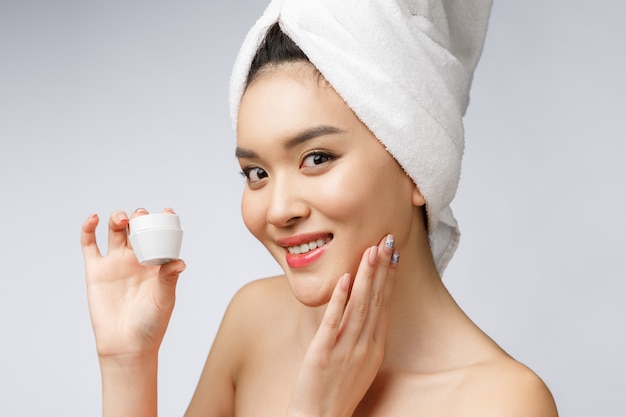 Health and beauty concept - Attractive asian woman applying cream on her skin, isolated on white.