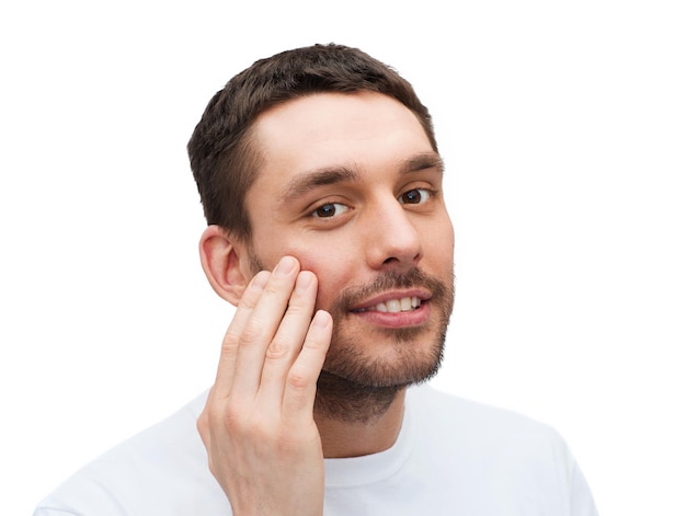 health and beauty concept - beautiful smiling man touching his face or applying cream