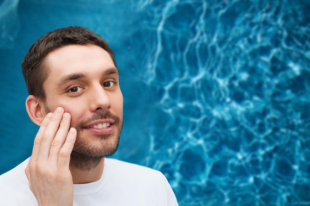 health and beauty concept - beautiful smiling man touching his face or applying cream