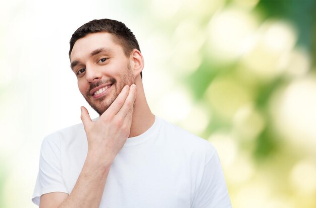 health and beauty concept - beautiful smiling man touching his face