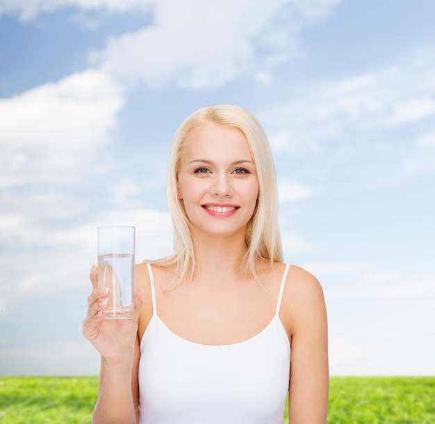 health and beauty concept - young smiling woman with glass of water