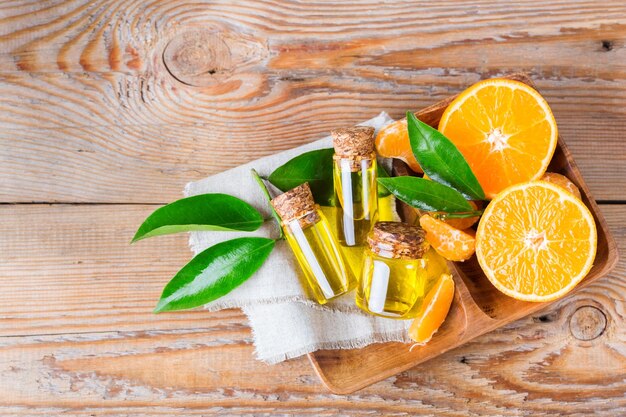 Health and beauty still life concept Organic essential tangerine mandarin clementine oil in a small glass jar and orange fruit on a rustic wooden table Copy space background top view