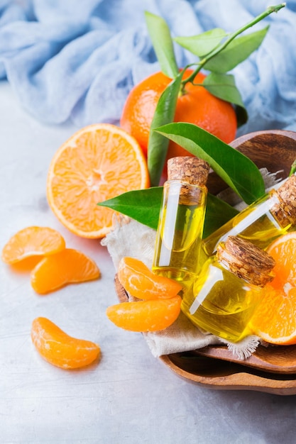 Health and beauty still life concept Organic essential tangerine mandarin clementine oil in a small glass jar with green leaves and orange fruit on a rustic table