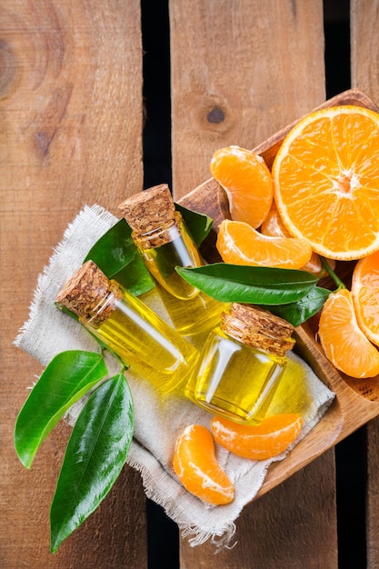 Health and beauty still life concept Organic essential tangerine mandarin clementine oil in a small glass jar with green leaves and orange fruit on a rustic wooden table