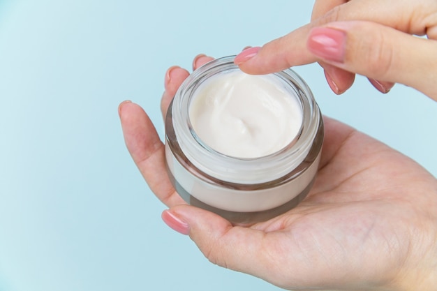 Health and beauty theme female hand holding a glass jar with white body care cream on background