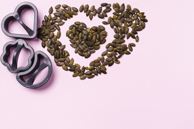 Health breakfast. Shape for cookies and a heart made of pumpkin seeds on pink background.