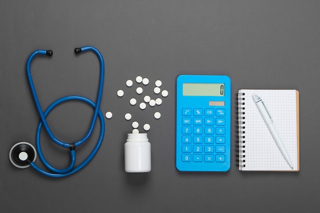 Health Care Concept. Calculator with a stethoscope, pills, notebook on gray.