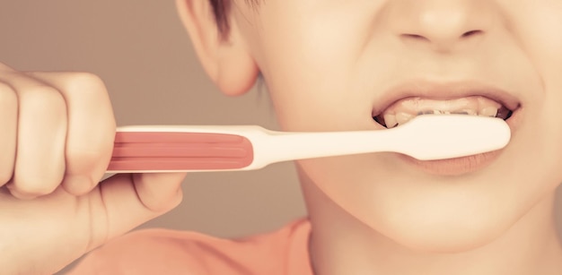 Assistenza sanitaria igiene dentale gioioso bambino mostra spazzolini da denti ragazzino che pulisce i denti ragazzino che si lava i denti ragazzo spazzolino da denti dentifricio bianco igiene dentale ragazzino felice che si lava i denti