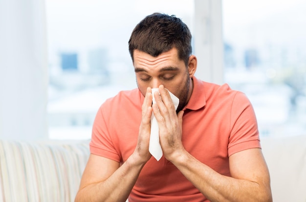 health care, flu, allergy, hygiene and people concept -sick man blowing nose to paper napkin at home