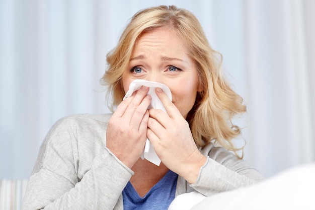 health care, flu, hygiene and people concept - ill woman blowing nose to paper napkin