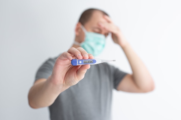 Health care, illness, virus and pandemic concept - sick man wearing protective mask with flu or coronavirus symptoms, headache and high temperature