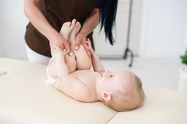 Health care and medical concept. A professional female masseuse makes a massage and gymnastics to a little baby at modern cozy room.