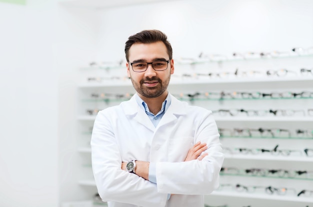 Concetto di assistenza sanitaria, persone, vista e visione - uomo ottico sorridente con occhiali e camice bianco al negozio di ottica