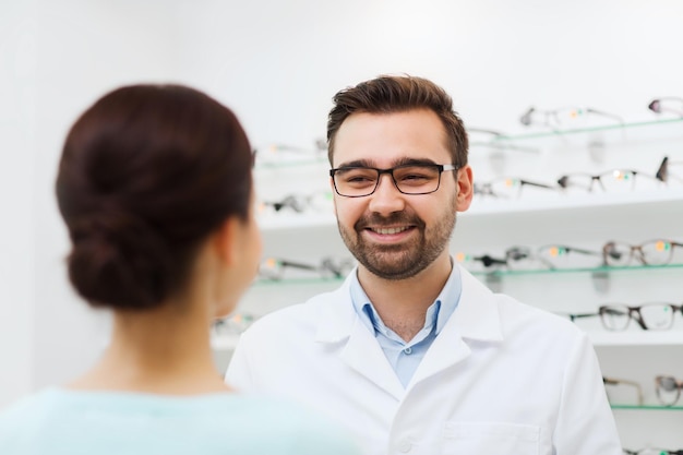 health care, people, eyesight and vision concept - woman and optician in glasses talking at optics store