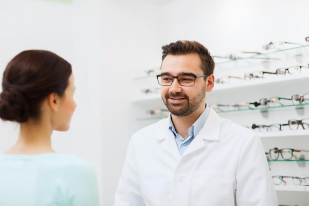 health care, people, eyesight and vision concept - woman and optician in glasses talking at optics store