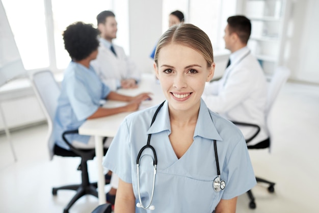 health care, profession, people and medicine concept - happy female doctor or nurse over group of medics meeting at hospital