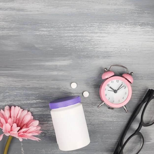 Health care style copy spaceplastic bottle with pills flowers clock and glasses on wood background