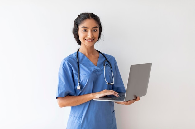 Health care and telemedicine smiling indian female doctor in uniform holding laptop