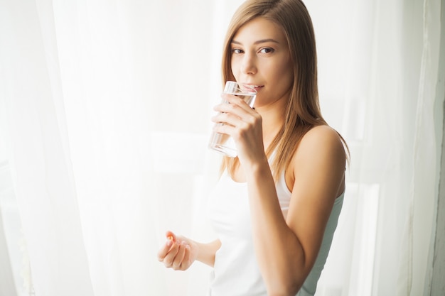 Health concept. Young woman holding pill and glass of water