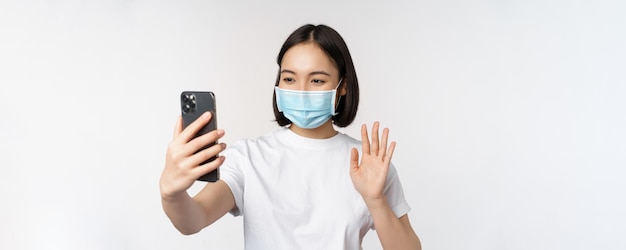 携帯電話の波と医療マスクビデオチャットで健康とcovidコンセプト現代アジアの女の子の学生