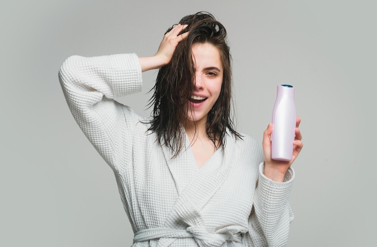 Photo health hair and beauty concept a beautiful young girl in the studio with wet hair with balm bottle beauty haircare cosmetics woman hold bottle shampoo and conditioner