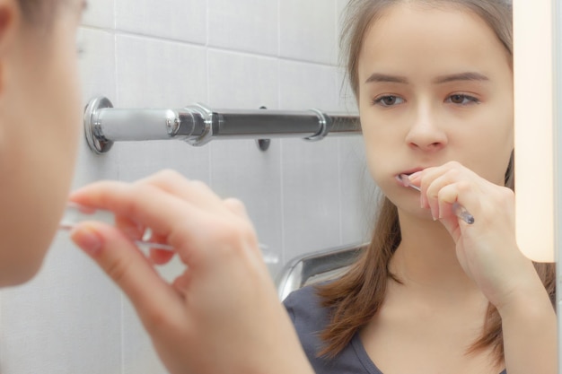 Health and hygiene. A girl brushes her teeth in front of a mirror in the bathroom.