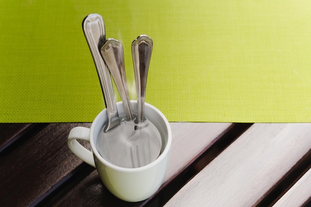 Health and hygiene soaking spoon and fork in hot water in cafe