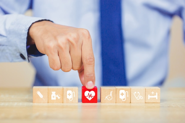 Foto concetto dell'assicurazione malattia, mano che organizza impilamento del blocco di legno con l'assistenza sanitaria dell'icona medica