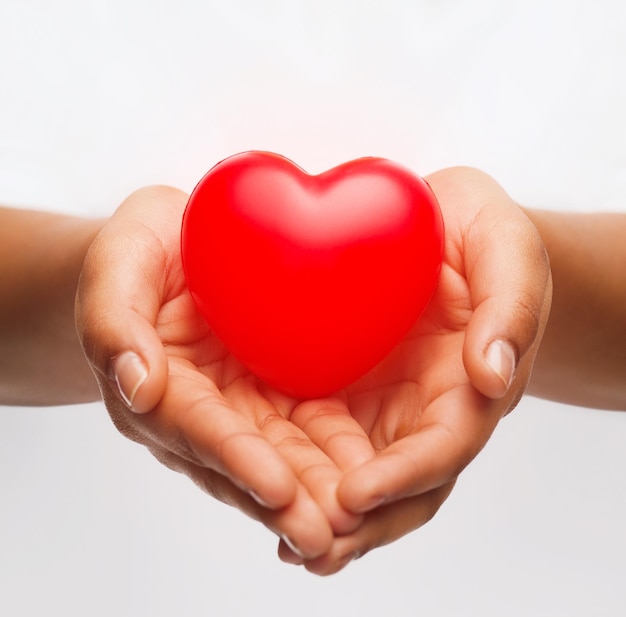 health, medicine and charity concept - close up of african american female hands with small red heart