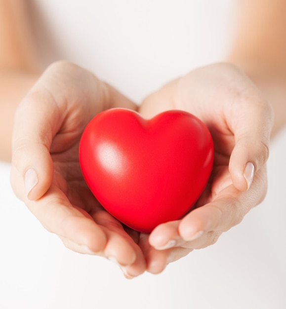 концепция здоровья, медицины и благотворительности - крупный план женских рук с маленьким красным сердцем