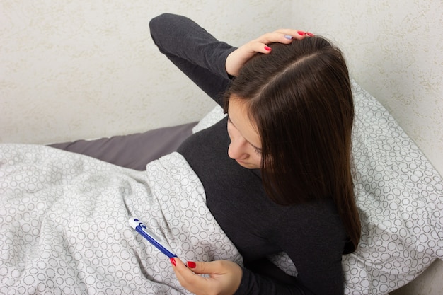 Health and medicine. a young girl is sick at home in bed, holds a thermometer.