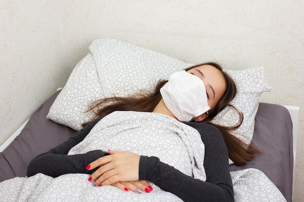 Health and medicine Young girl is sick at home in bed lies in an antiviral mask