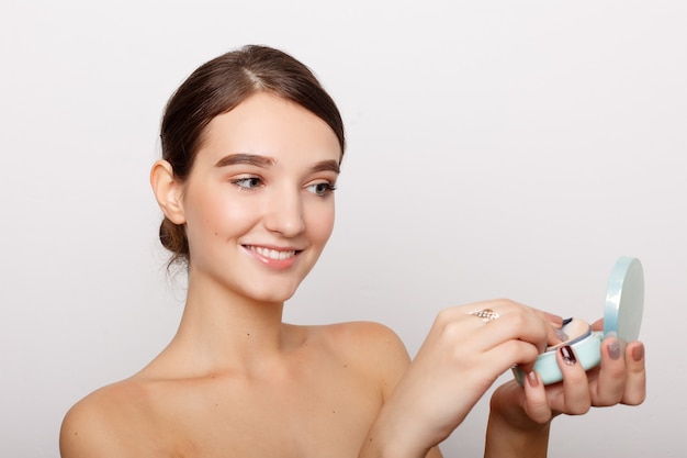 Health, people and beauty concept - Young woman applying blusher on her face with powder puff, skin care concept, photo composition of brunette girl, isolated on white background