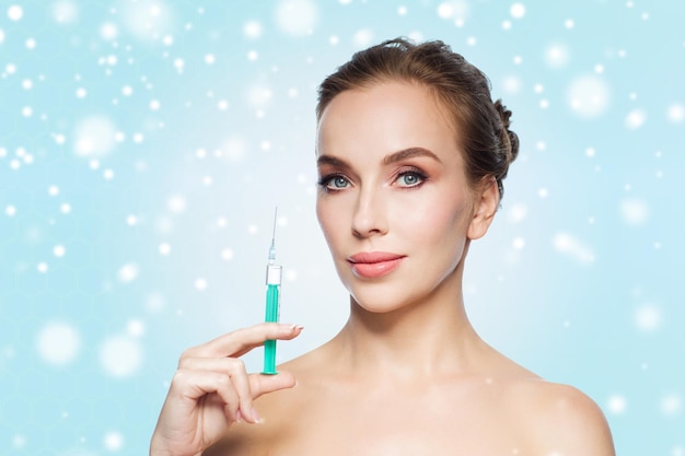 health, people, cosmetology, plastic surgery and beauty concept - beautiful young woman holding syringe with injection over blue background and snow