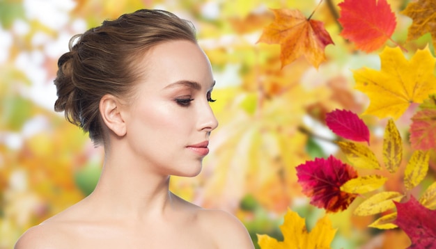 health, people, season and beauty concept - beautiful young woman face over autumn leaves background