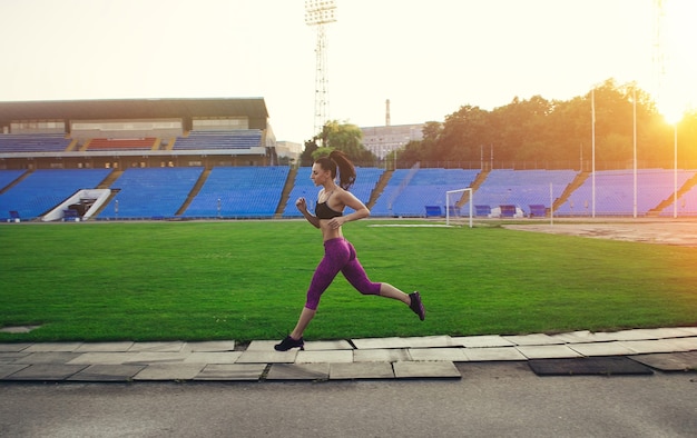 Health, people, Sport and lifestyle concept - Slim athletic woman run in the stadium. Sporty sexy girl with flat belly workout, outdoors. red highlight on the background