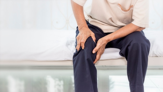 Фото Концепция проблемы со здоровьем; старая женщина страдает от боли в колене в домашних условиях.