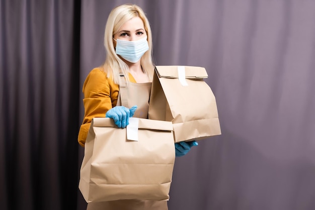 health protection, safety and pandemic concept - delivery woman in face protective mask and gloves holding parcel box and over warehouse background.