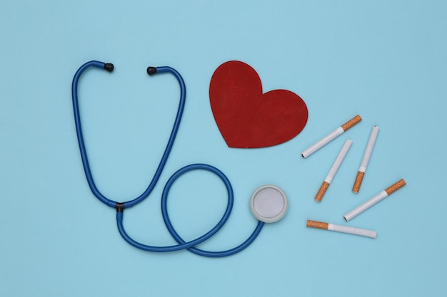 The health risks of smoking. Diagnosis of the disease. Stethoscope and cigarettes, heart on blue background. Quitting smoking